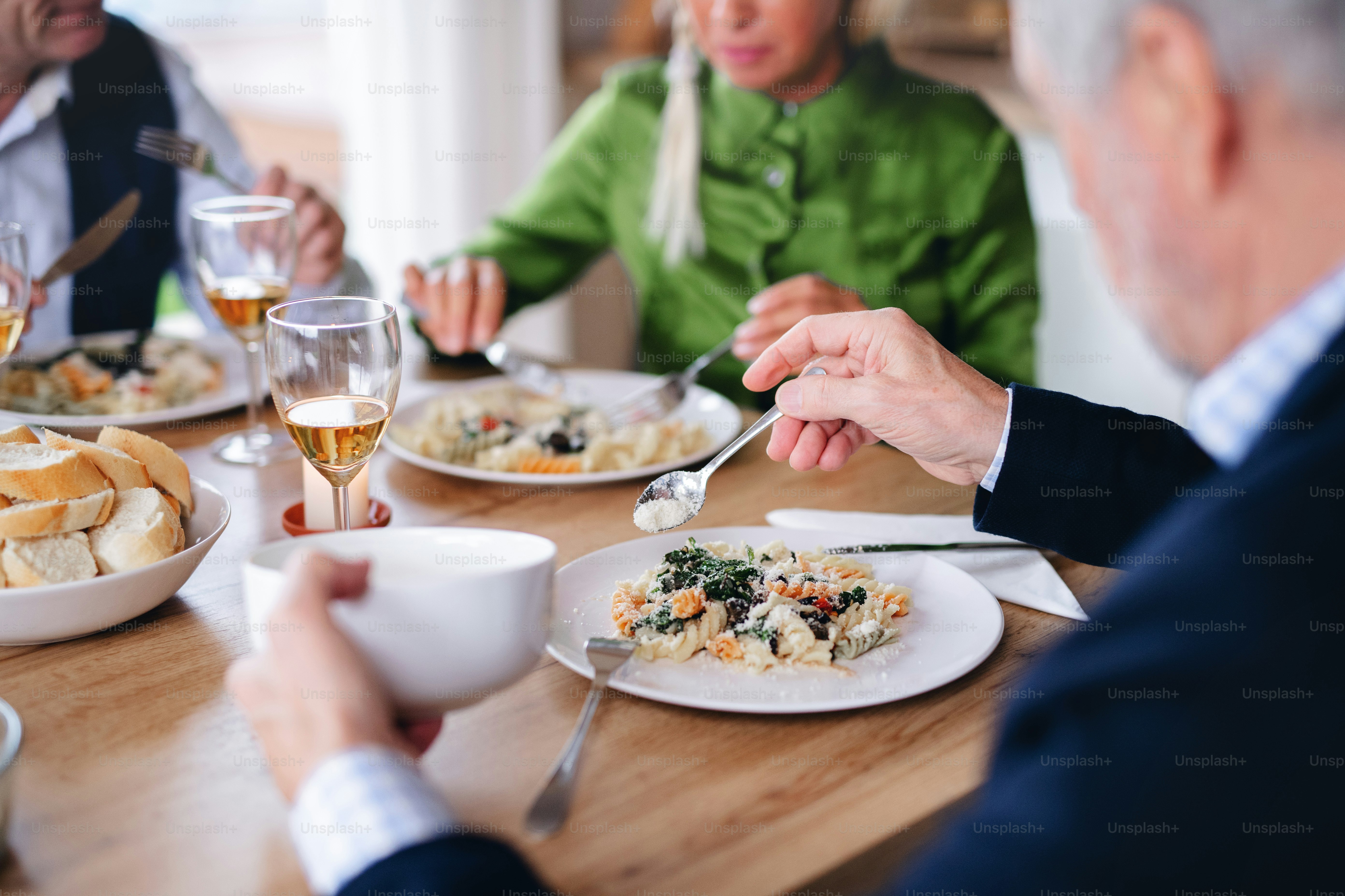 Gruppo di amici anziani irriconoscibili che si godono la cena a casa, mangiando.