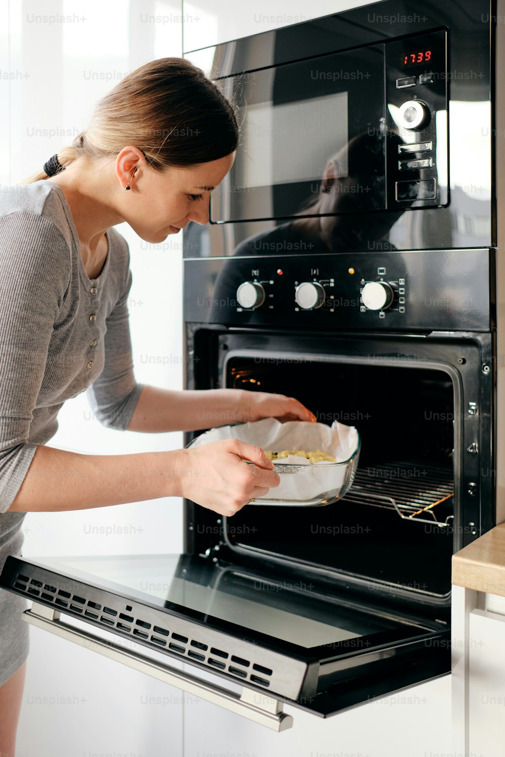 Attractive awesome girl putting baking sheet pie in oven while day light reflects on her body