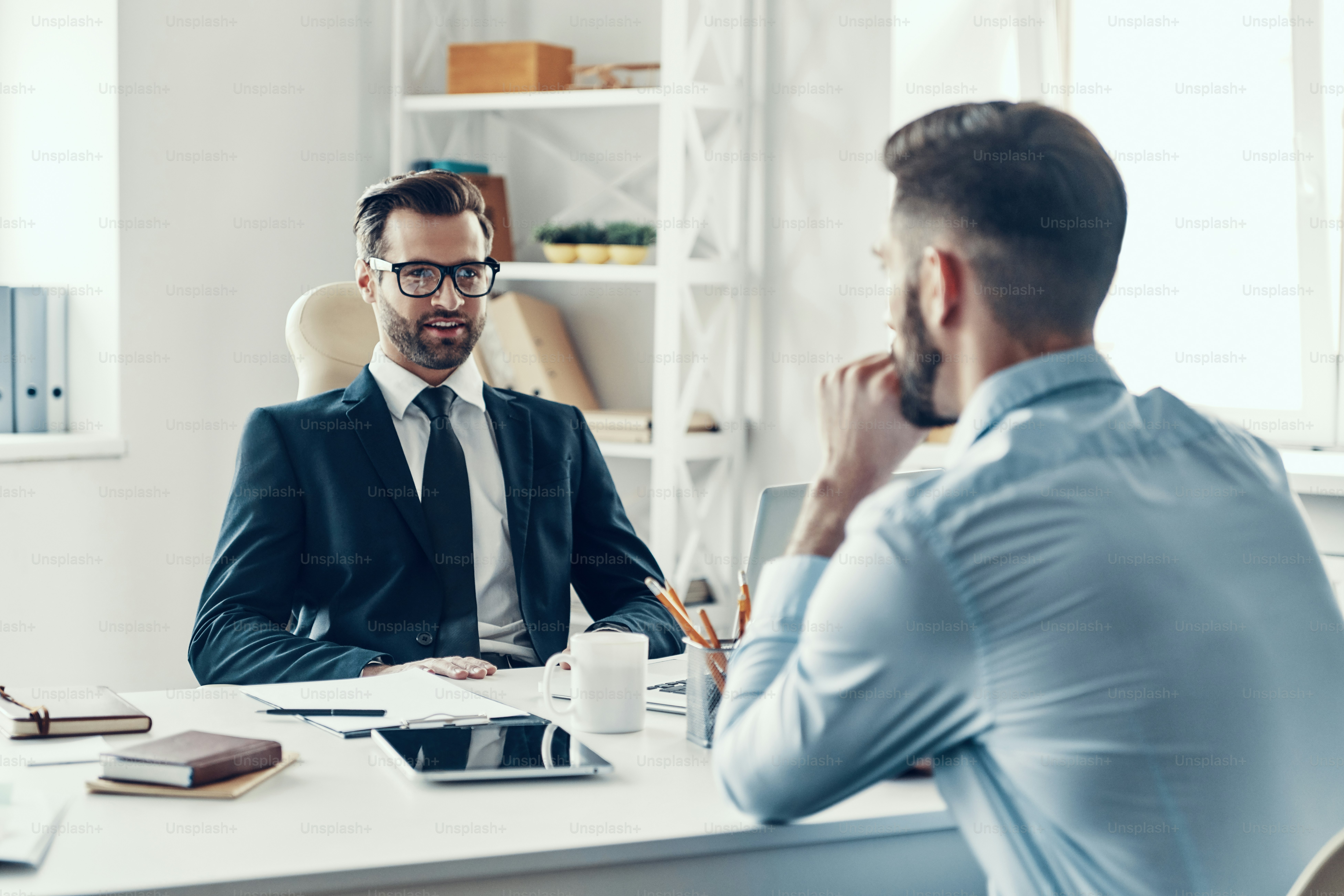 Two young men in formalwear communicating together while sitting in the office