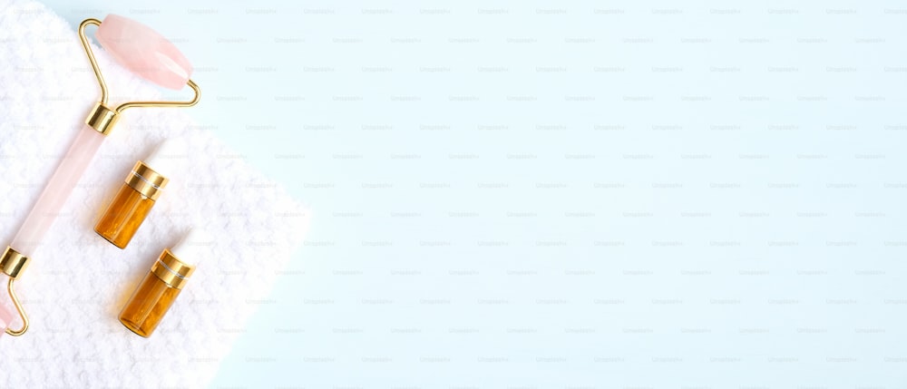 Rodillo facial de cuarzo rosa y aceite esencial sobre fondo azul. Masajeador facial, herramienta de cuidado de la piel de belleza antienvejecimiento y antiarrugas. Plano plano, vista superior, espacio de copia