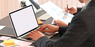 モダンなオフィスを背景に、黒いミーティングテーブルに一緒に座りながら、コンピューター、タブレット、ラップトップ、グラフィックチャートで一緒に作業するビジネスマンのトリミングされた画像。