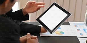 Cropped image of business people working together with computer tablet and graphic charts while sitting together at black meeting table over modern office as background.