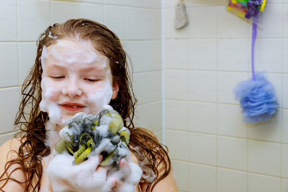 Jolie petite fille se baignant dans un bain de mousse se lavant les cheveux