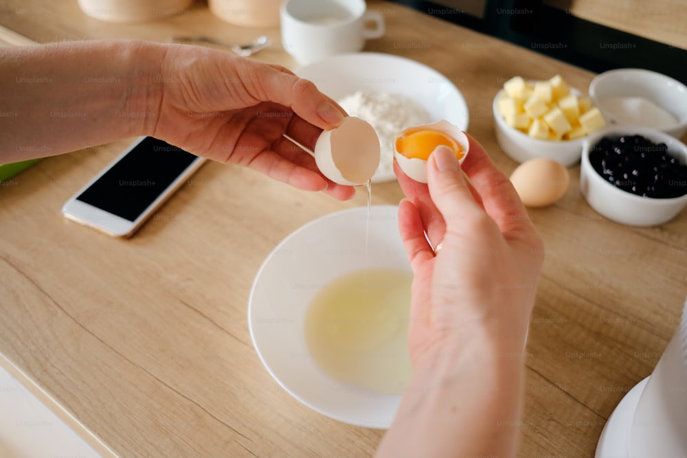 Mãos de mulher de perto quebrar ovos de galinha em um prato na cozinha. Massa de cozinha.