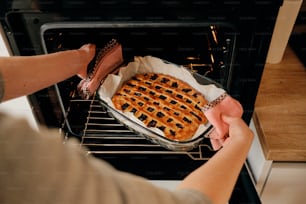 Woman hand taking baking tray with delicious pie from oven.