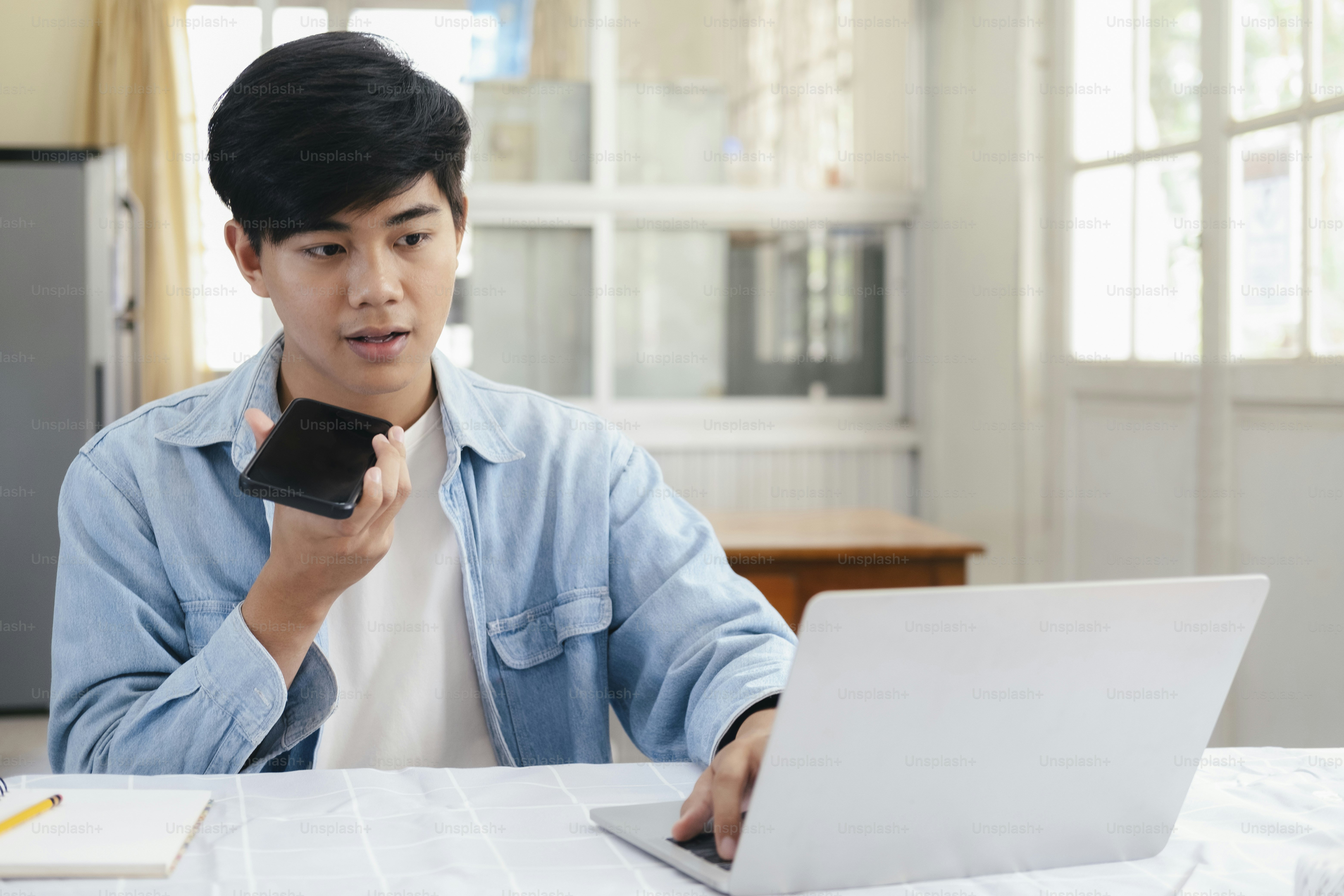 Young man talking on the phone with handfree and using laptop working and meeting online at home.
