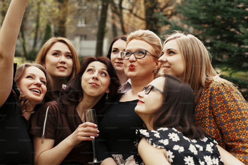 Donne eleganti alla moda che prendono selfie divertenti alla celebrazione soleggiata nel parco, concetto di vita felice di lusso