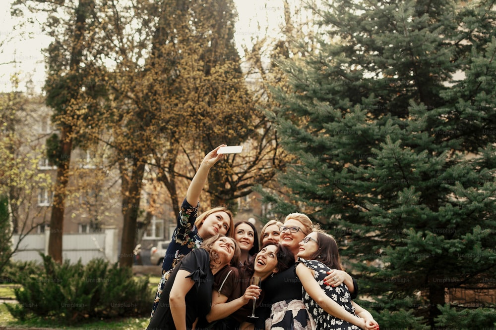 mulheres elegantes e elegantes tirando selfie engraçada na celebração ensolarada no parque, conceito de vida feliz de luxo