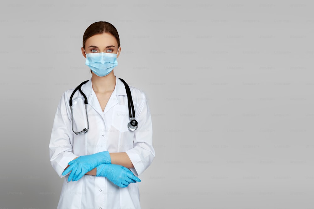 Porträt einer schönen Ärztin in weißem Laborkittel, Maske und Gummihandschuhen und Stethoskop isoliert auf grauem Hintergrund. Speicherplatz kopieren