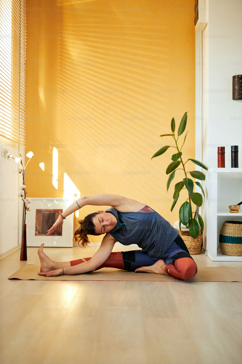 Attractive flexible Caucasian yoga brunette in Revolved Head to Knee yoga pose. Home interior, morning time.
