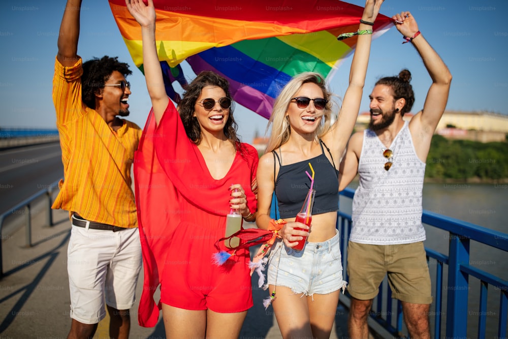 Glückliche Gruppe von Menschen, Freunde, die in der Stadt herumhängen und LGBT mit Pride-Flagge schwenken