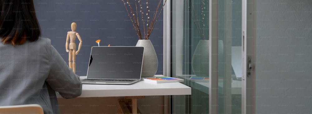 Abgeschnittene Aufnahme eines professionellen Designers, der im trendigen Büroraum mit Laptop und Designerzubehör auf einem weißen Tisch arbeitet