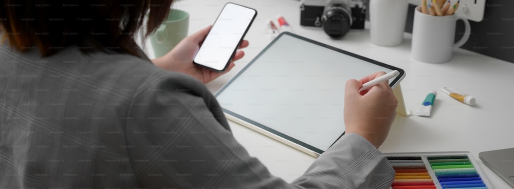 Beschnittene Aufnahme einer Designerin, die an digitalen Mock-up-Geräten und Designerzubehör auf einem weißen Tisch arbeitet