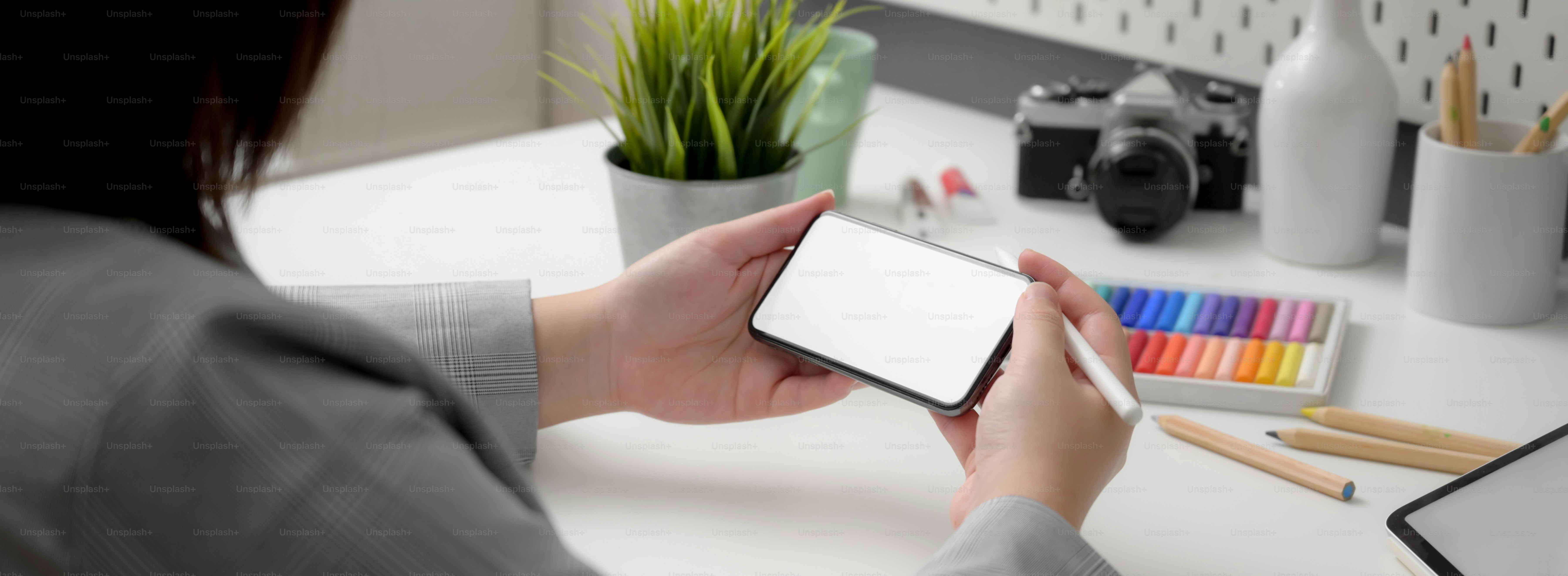 Cropped shot of professional designer using horizontal mock-up  smartphone while sitting at minimal workspace with designer supplies