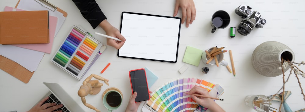 Top view of two designers working together with digital devices while sitting opposite each other at comfortable workspace