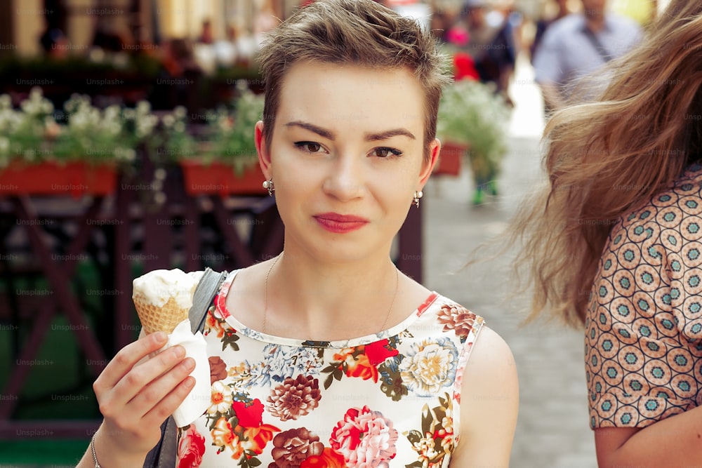 Mujer feliz con estilo que sostiene helado de vainilla en las manos, fiesta en la calle de la ciudad, momentos alegres