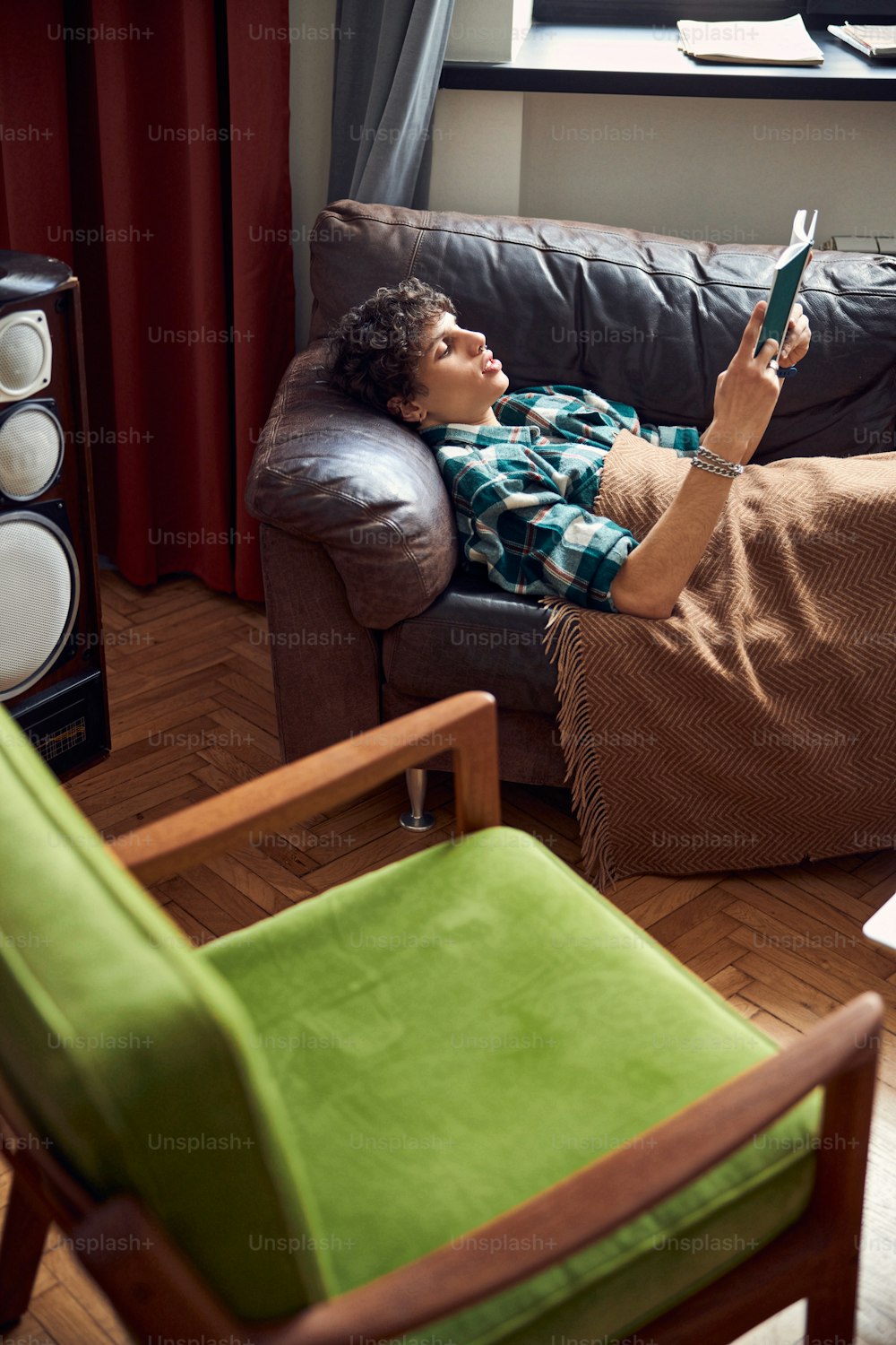 Lockiger Kerl, der auf der Couch liegt und ein interessantes neuartiges Stockfoto genießt