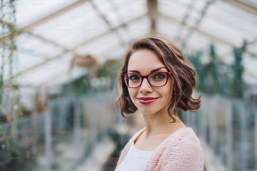 Young woman researcher standing in greenhouse in botanical garden, looking at camera.