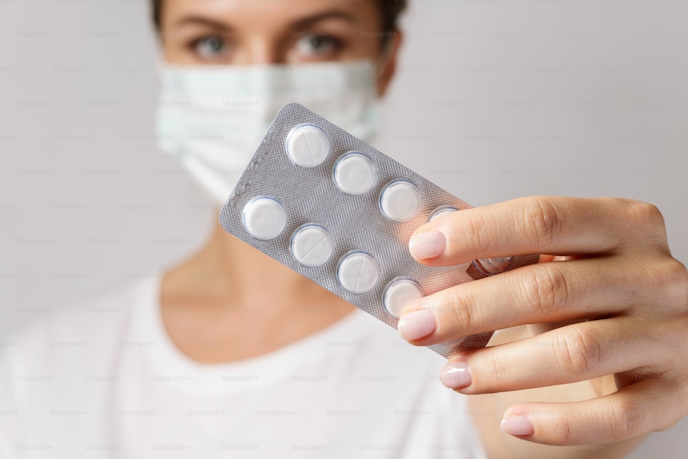 Young woman wearing face mask is holding a white pills