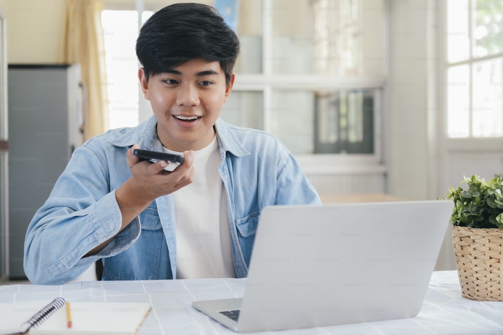 Joven hablando por teléfono con manos libres y usando una computadora portátil trabajando y reuniéndose en línea en casa.