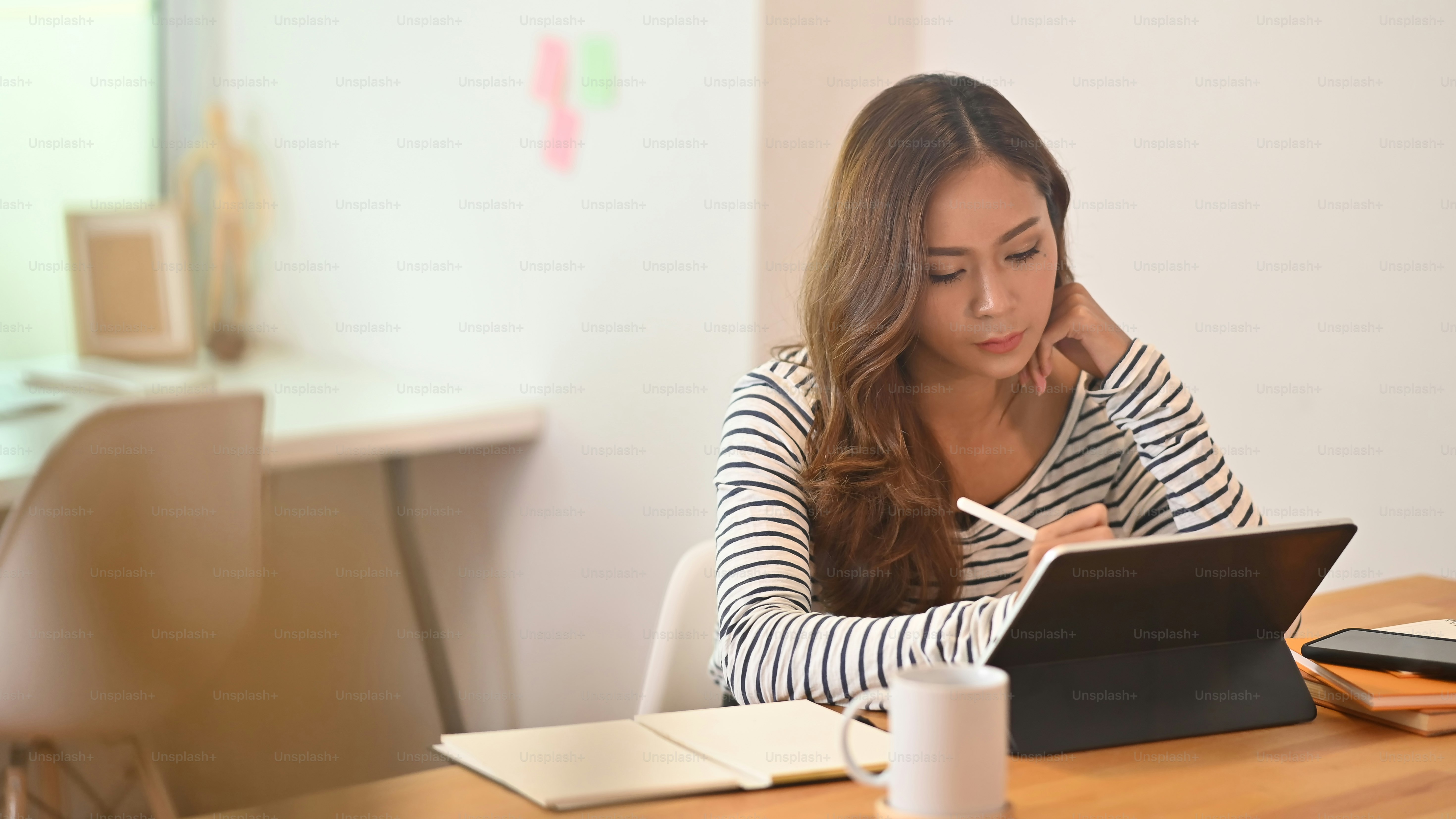 Photo of beautiful creative woman using a stylus pen to drawing on computer tablet with keyboard case that putting on working desk while sitting in orderly living room.
