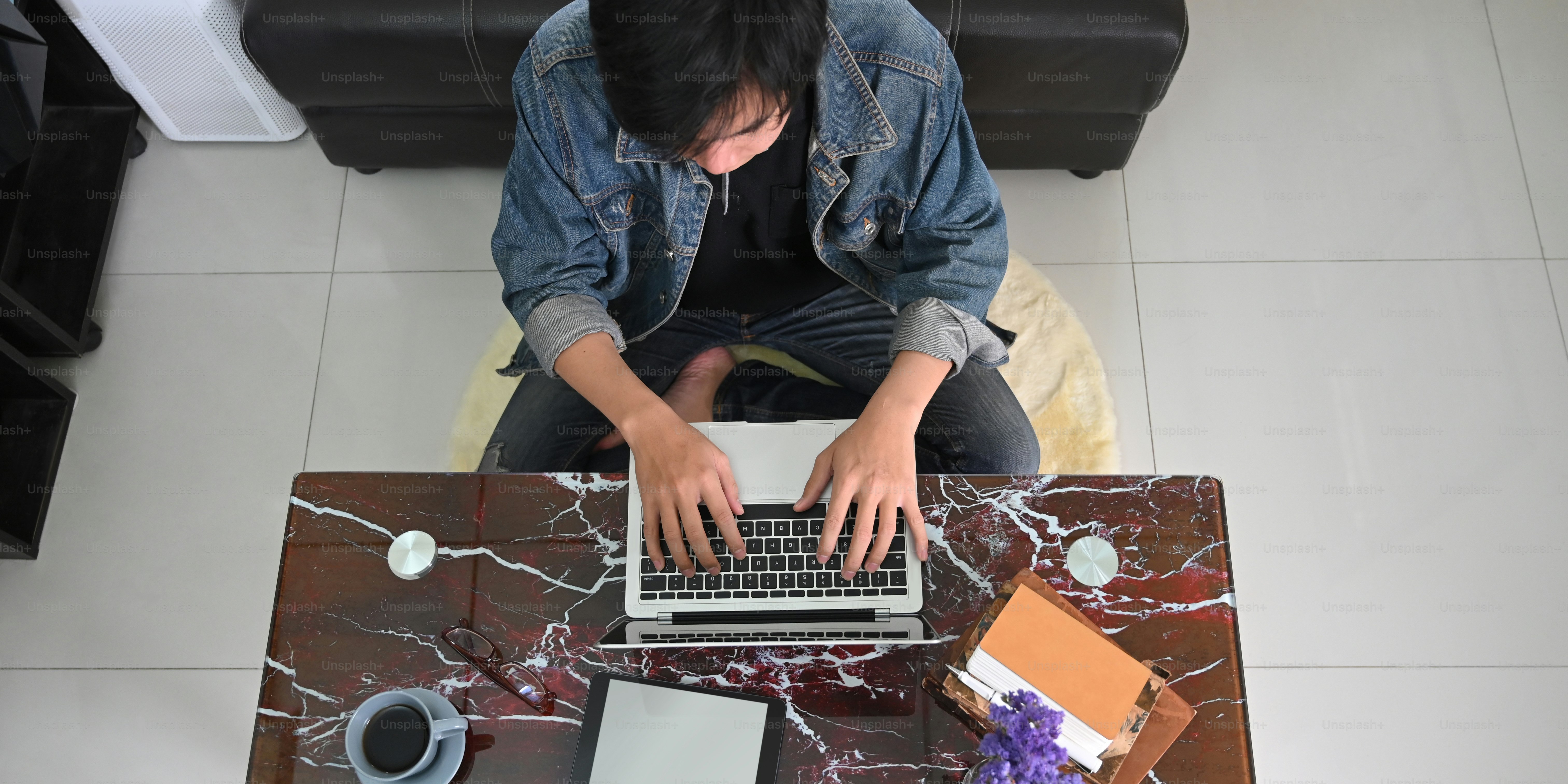 Top view image of smart man working as graphic design while sitting at the marble texture desk and typing on his computer laptop over comfortable living room as background.