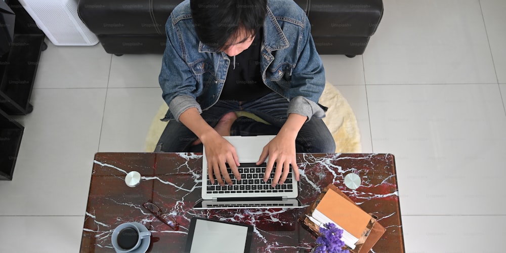 Image de vue de dessus d’un homme intelligent travaillant comme graphiste tout en étant assis au bureau de texture de marbre et en tapant sur son ordinateur portable au-dessus d’un salon confortable comme arrière-plan.