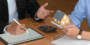 부동산 중개인의 자른 이미지는 현대적인 나무 테이블에서 파란색 셔츠를 입은 똑똑한 남자에게 주택 보험 또는 주택 소유권을 제공합니다. 계약에 서명, 브로커/판매자/딜러 개념.