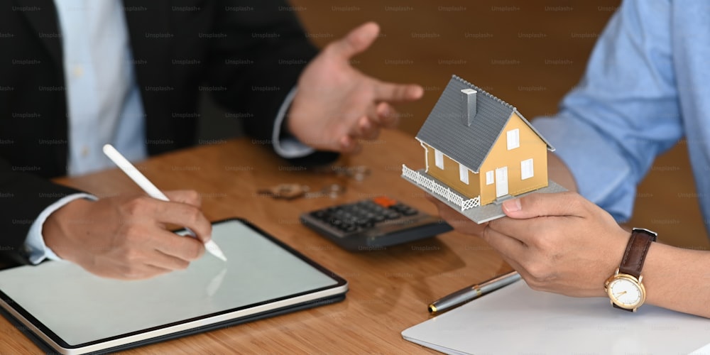 Abgeschnittenes Bild von Immobilienmakler bieten Hausversicherung oder Hausbesitz zu klugen Mann in blauem Hemd "n am modernen Holztisch. Vertragsunterzeichnung, Broker/Verkäufer/Händler-Konzept.