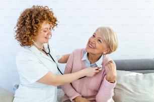 Visiteur de santé et une femme âgée lors d’une visite à domicile. Jeune femme médecin examinant un patient âgé. Jeune femme médecin portant une blouse blanche examinant une femme âgée.