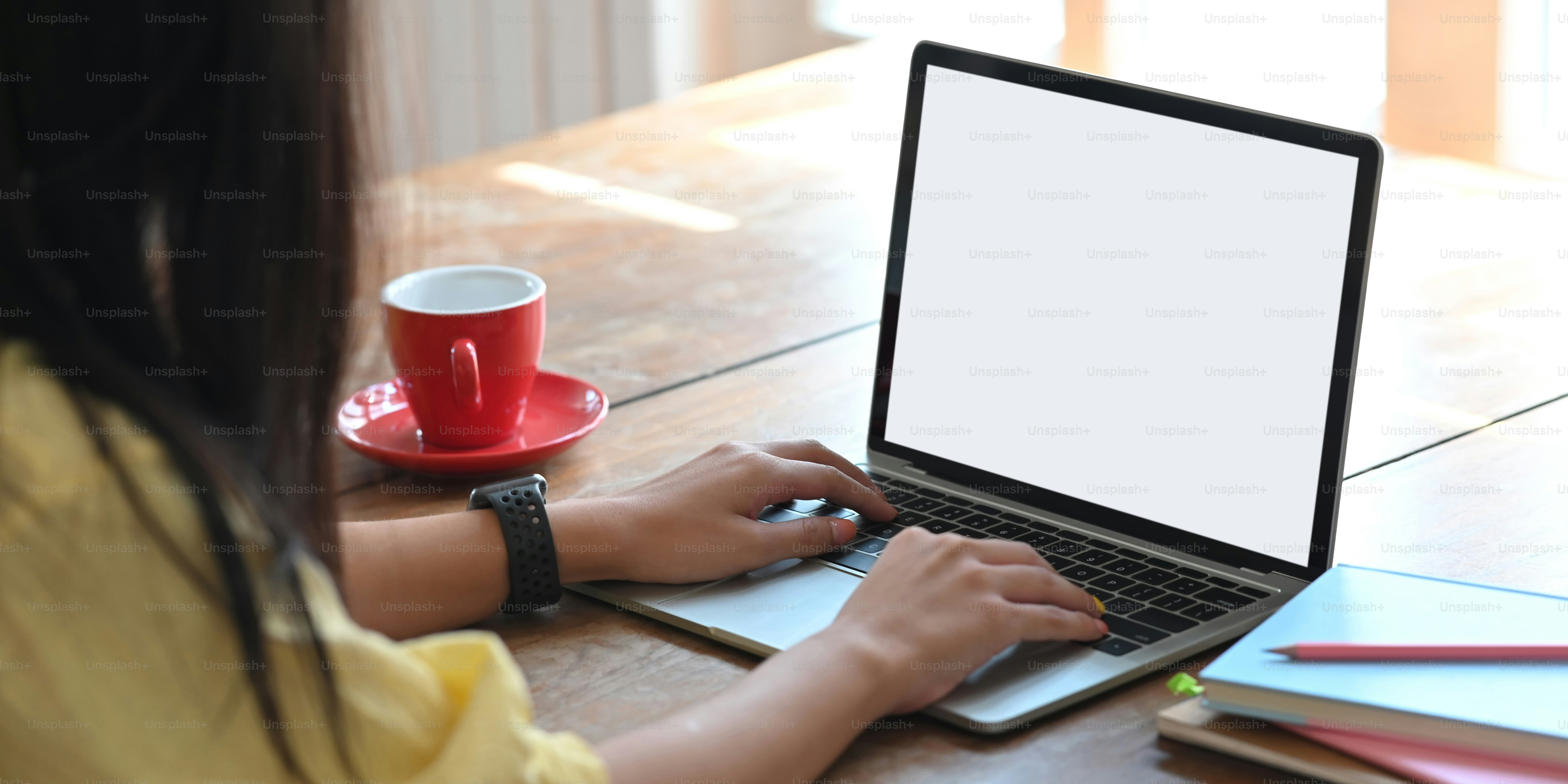 Imagen recortada de una hermosa mujer escribiendo en una computadora portátil con una pantalla blanca en blanco que se pone en el escritorio de trabajo y rodeada de una computadora portátil y una taza de café sobre una cómoda sala de estar como fondo.