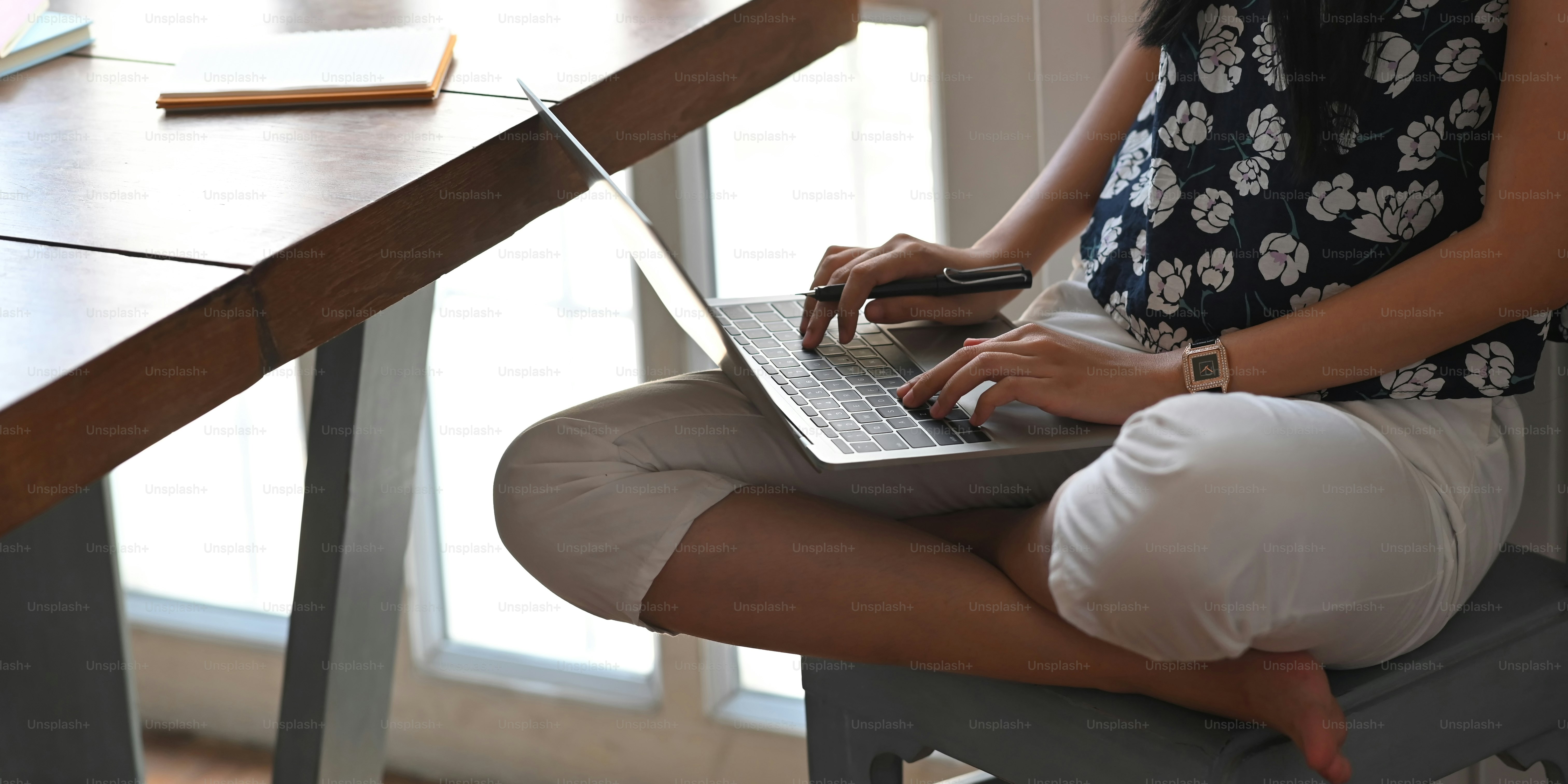 Imagen recortada de una hermosa mujer escribiendo en una computadora portátil que se pone en su regazo mientras está sentada en el escritorio de trabajo de madera sobre una cómoda sala de estar como fondo.
