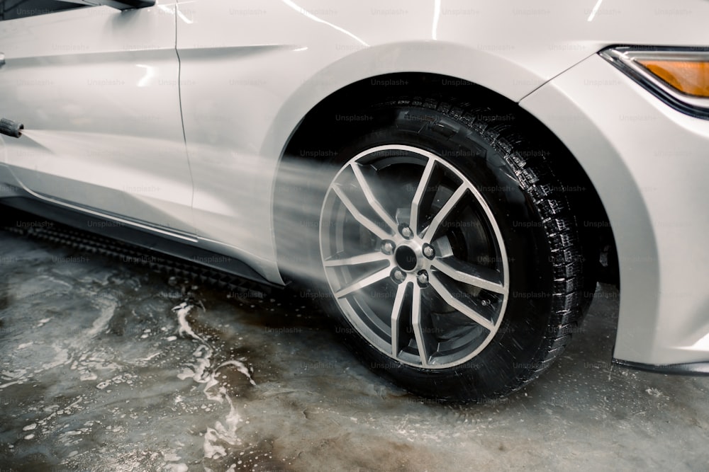 手洗い、カーディテーリング。水鉄砲で車の車輪を掃除するプロセスのクローズアップ画像。車のリムは高圧水を使用して洗浄します。手動砥石洗浄コンセプトの詳細