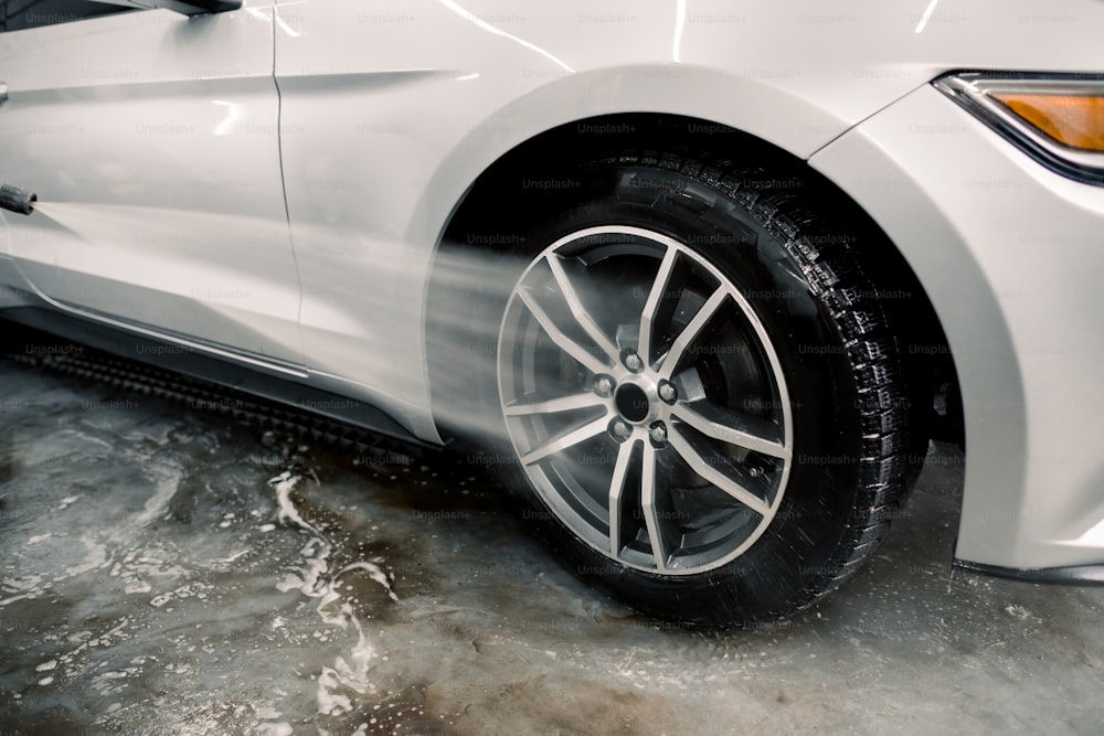 Washing a car by hand, car detailing. Close up image of the process of cleaning the car wheels with a water gun. Car rims wash using high pressure water. Detail of manual wheel cleaning concept