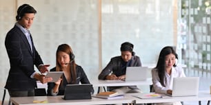 Call center/operator/call service team while working and sitting together at the long working desk over comfortable office as background.