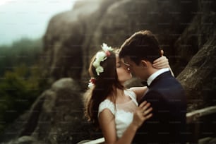 luxury happy bride and stylish groom kissing on background of  view of sunny rocks in amazing mountains