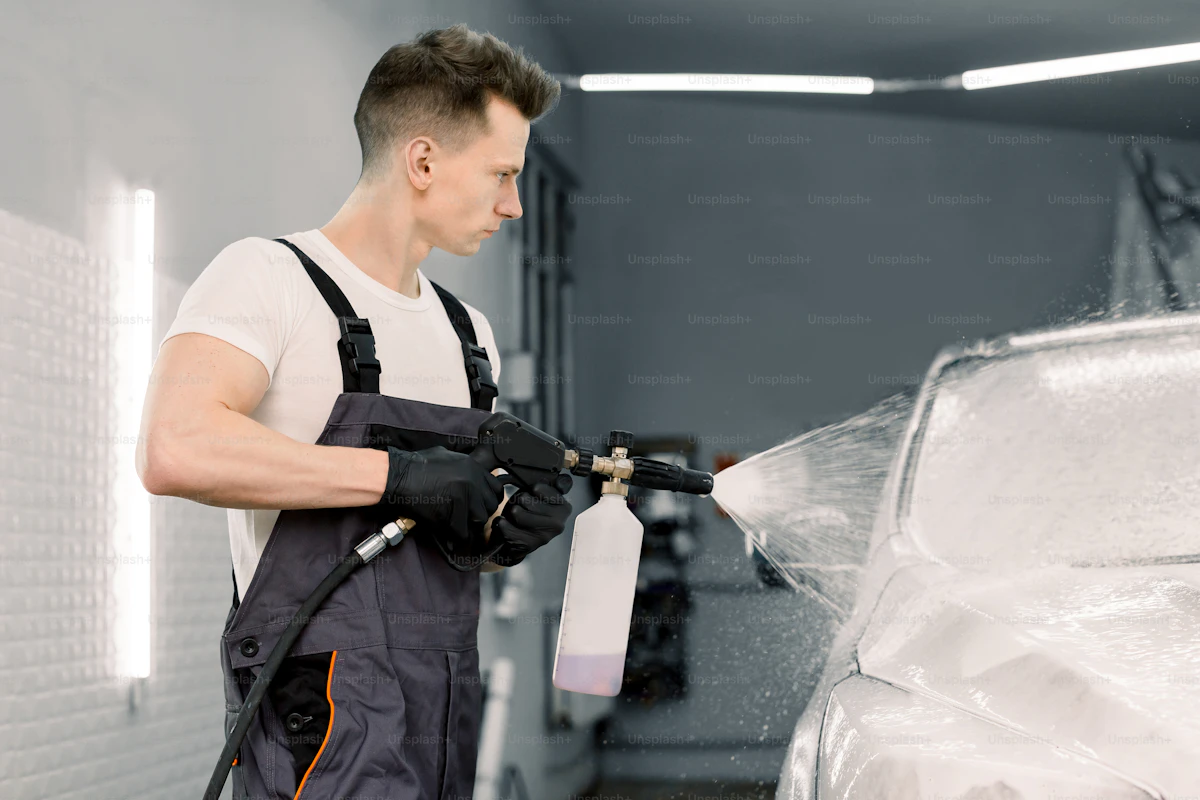 Car wash employee spraying a vehicle with high pressure foam and water