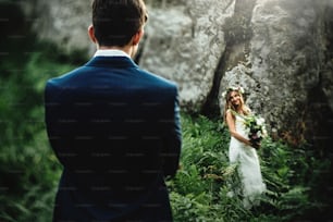 stylish boho bride holding and elegant happy groom on background of rocks in mountains