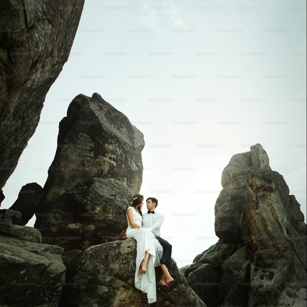 happy beautiful bride and elegant stylish groom  hugging on rocks on the background of sunset mountains
