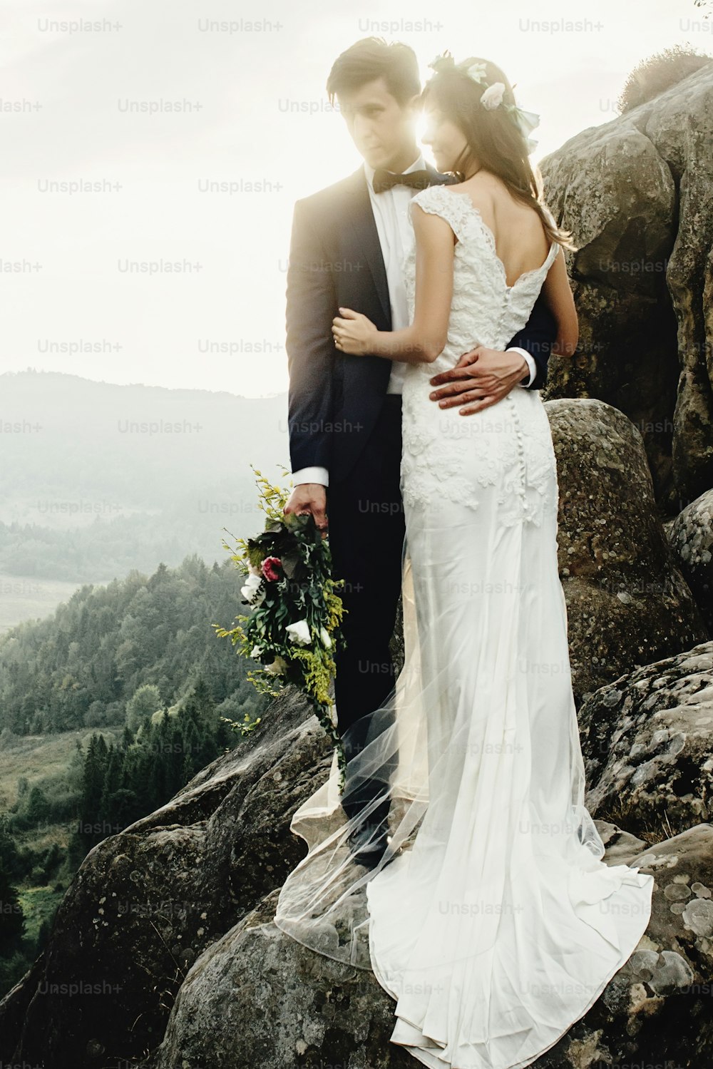 stylish gorgeous couple newlyweds standing on the rocks in the mountains in the evening light