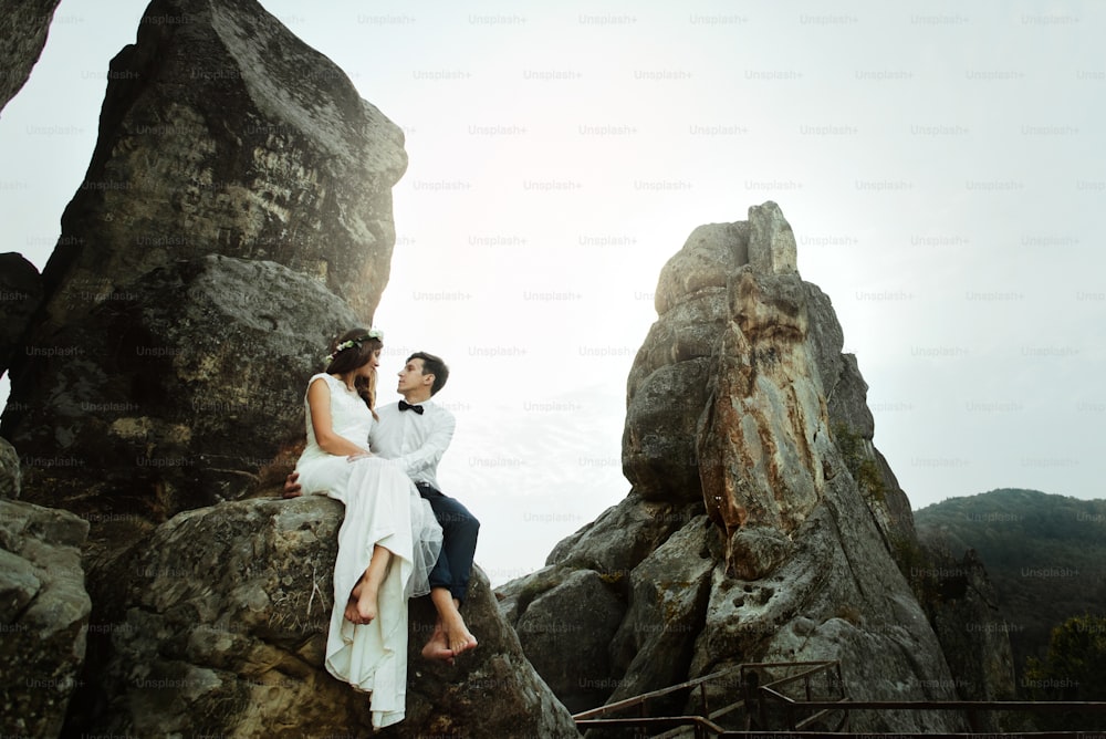 noiva bonita feliz e elegante noivo elegante abraçando em rochas no fundo das montanhas do pôr do sol