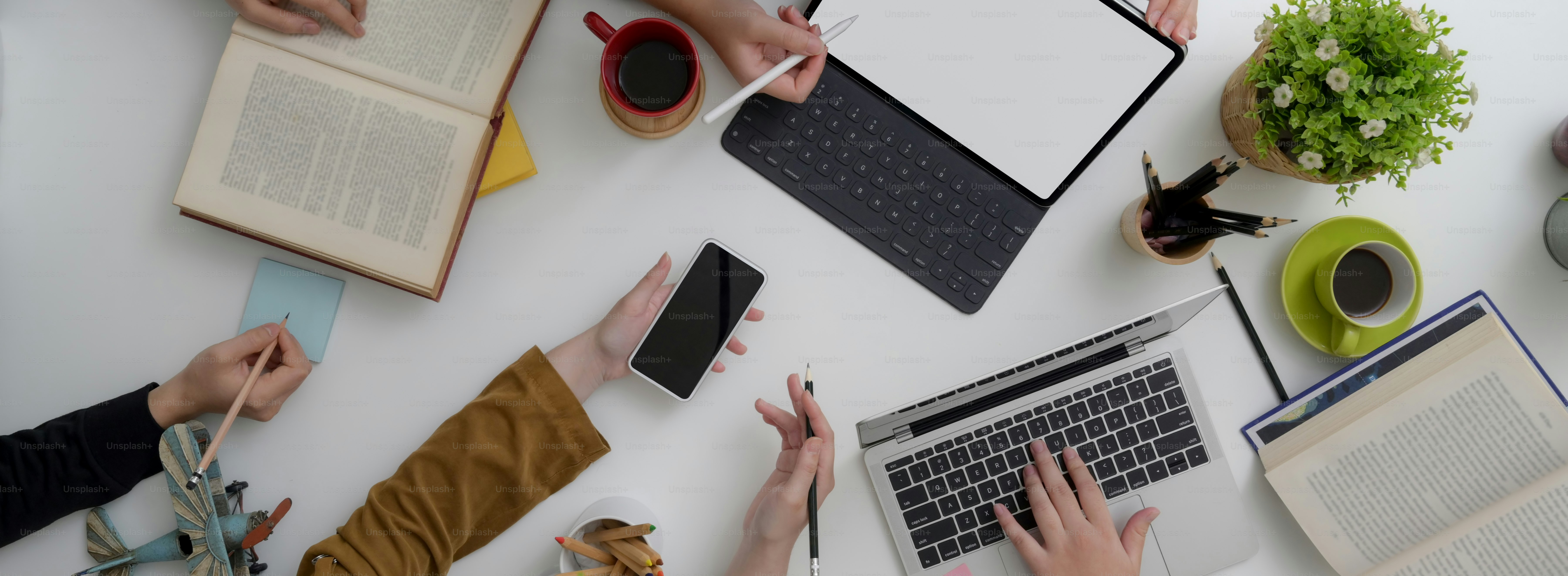 Top view of university student group consulting on their thesis with digital devices and books on white table in co-working space