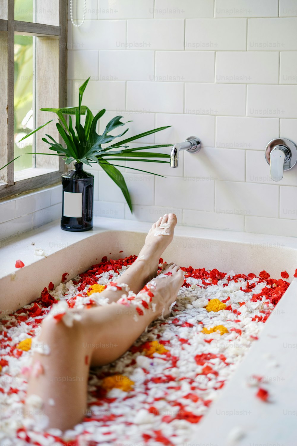 Vertical and cropped view of young adult woman lying in bathtub with tropical flowers, relaxing in bathroom, enjoying spa procedure and morning routine in hotel