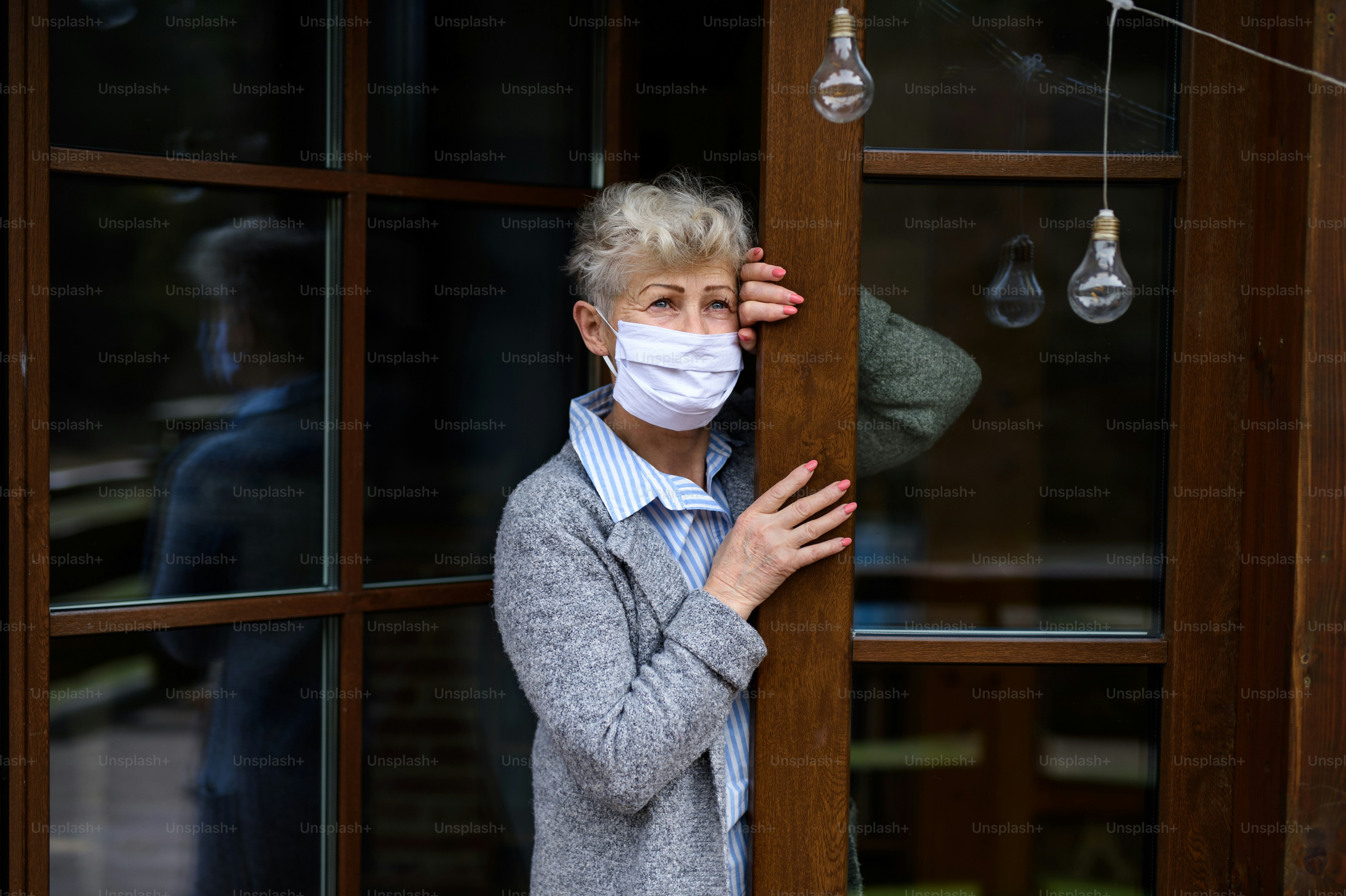 Idosa triste e deprimida parada na porta da frente de casa, corona vírus e conceito de quarentena.