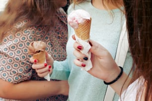 アイスクリームを手に。チョコレートとピンクのアイスクリームを手にクローズアップし、パーティーをして街の通りで楽しんでいる女性のグループ