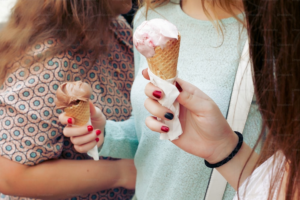 ice cream in hand. Group of women holding chocolate and pink ice-cream in hands close-up, partying and having fun  in city street