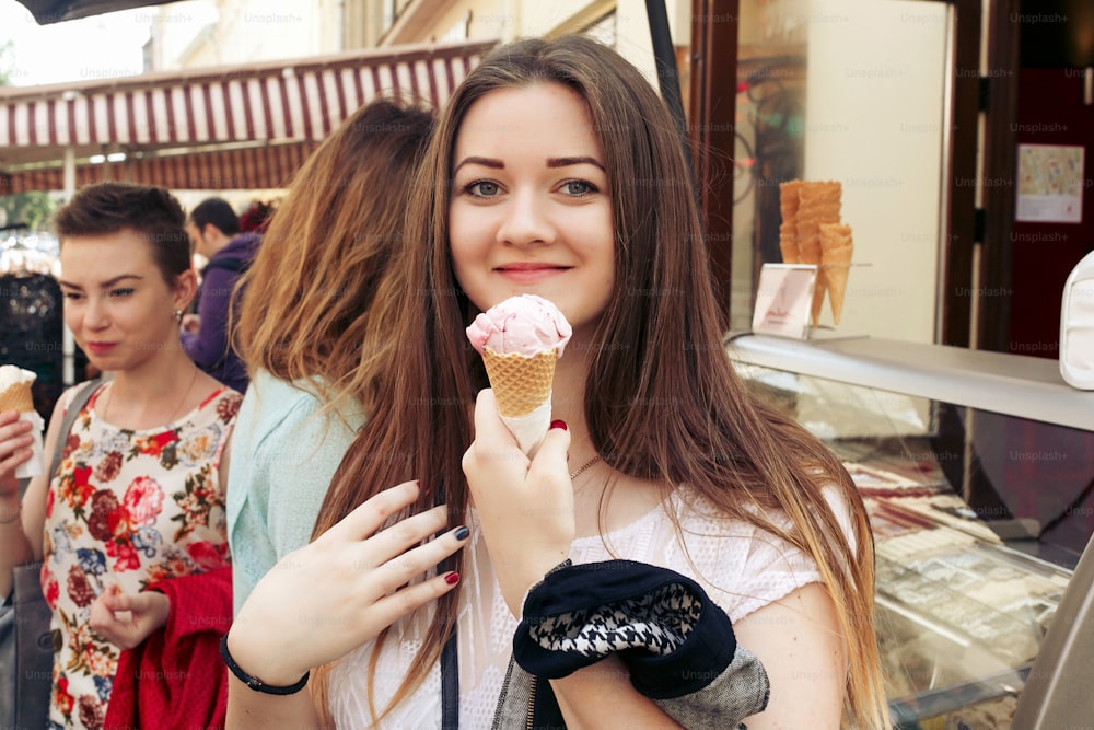 donna felice alla moda che tiene il gelato alla fragola in mano, festa nella strada della città, momenti gioiosi