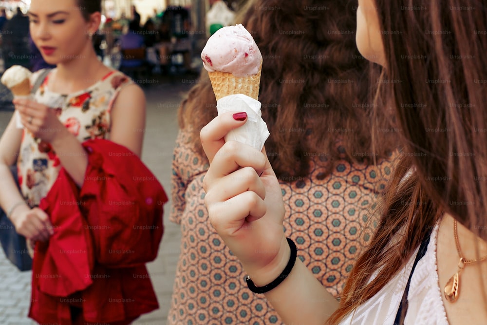 sorvete na mão. Grupo de mulheres segurando chocolate e sorvete rosa nas mãos de perto, festejando e se divertindo na rua da cidade