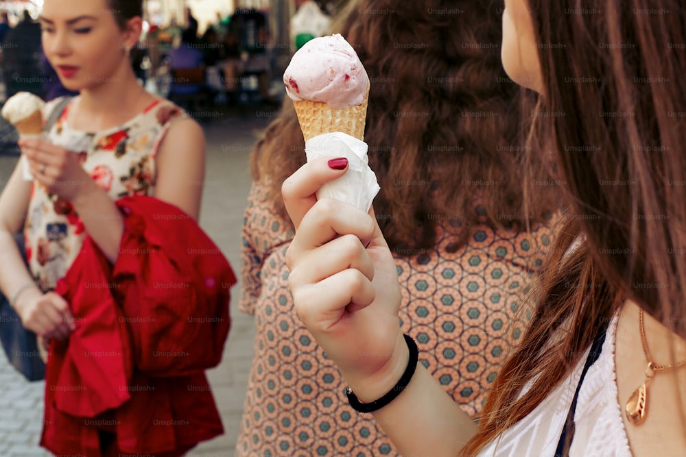 ice cream in hand. Group of women holding chocolate and pink ice-cream in hands close-up, partying and having fun  in city street