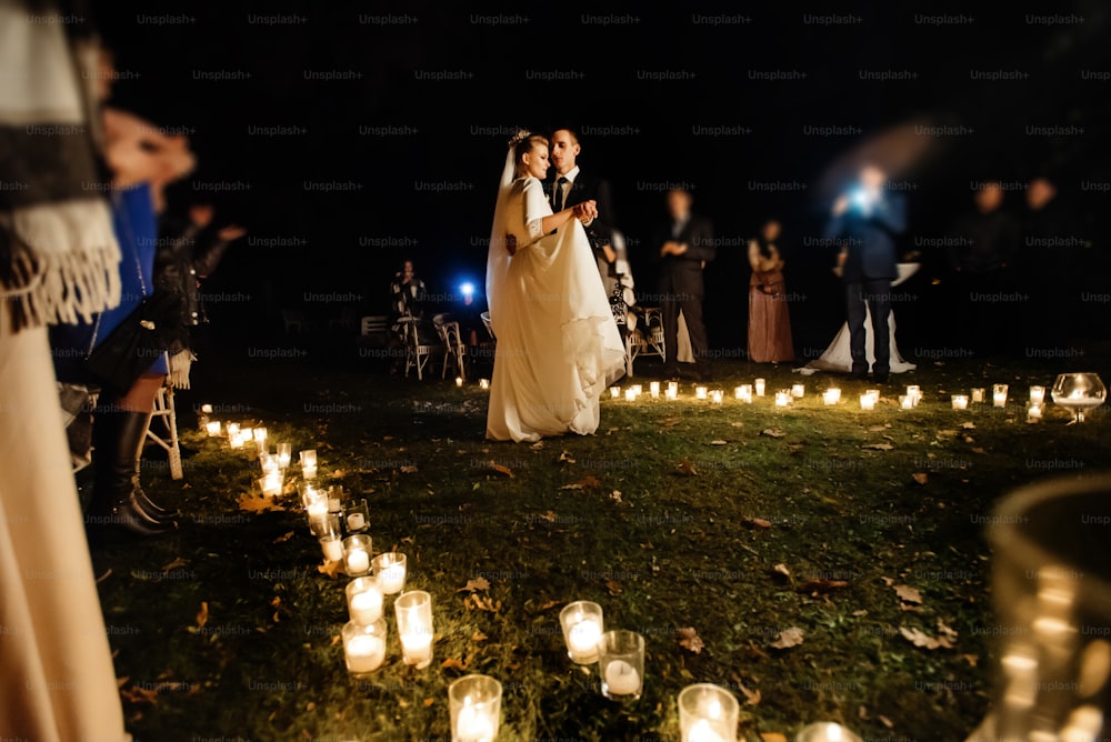 화려한 신부와 세련된 신랑이 저녁 결혼식에서 낭만적인 촛불에서 첫 춤을 추고 있다